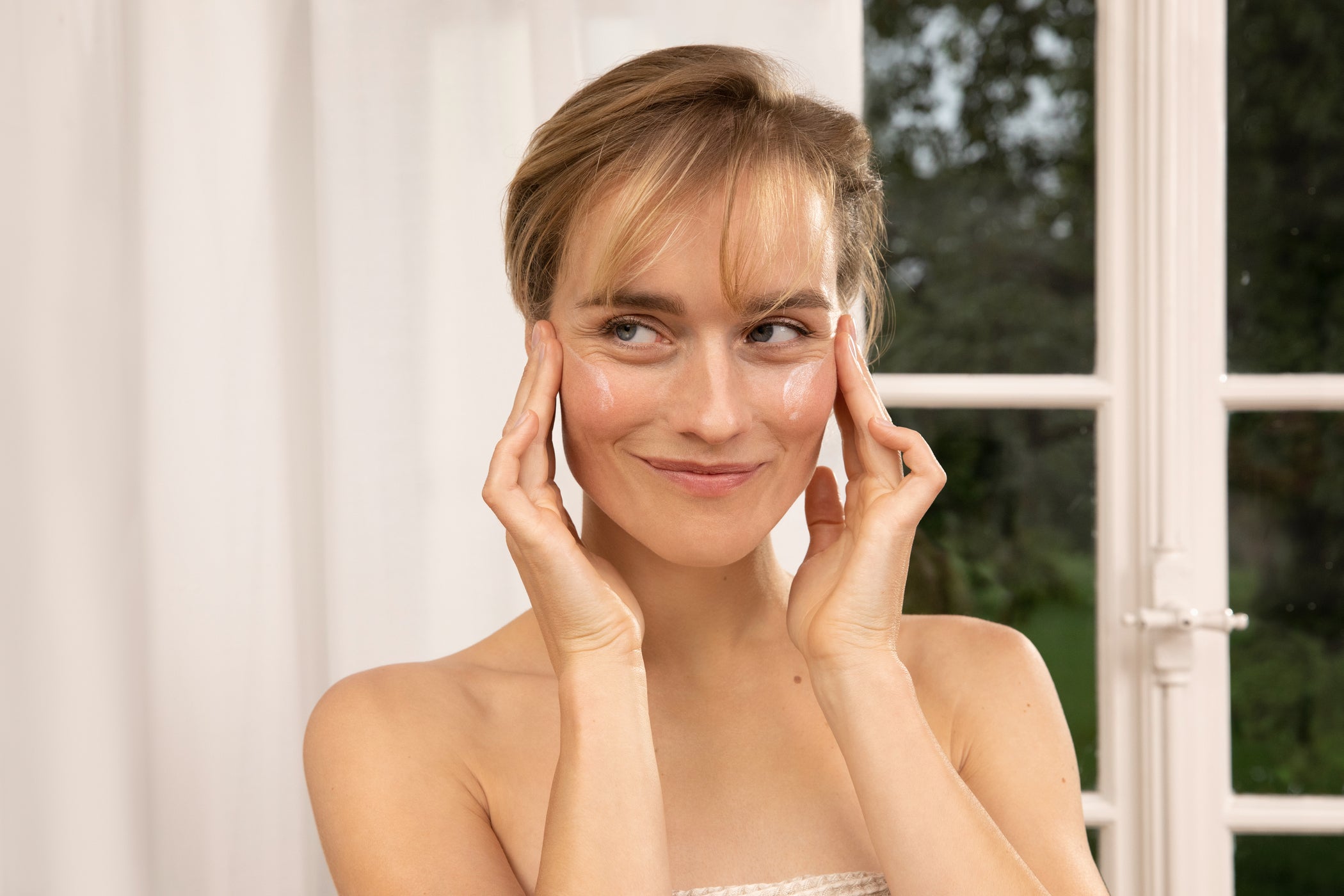 Blonde Frau trägt sich Sonnenschutz im Gesicht auf