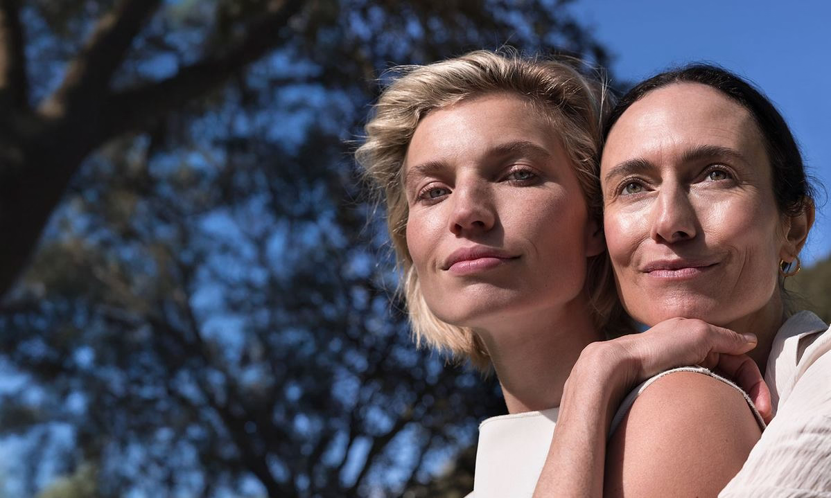 Zwei Frauen in der Sonne, eine umarmt die andere, natürlicher Look im Freien