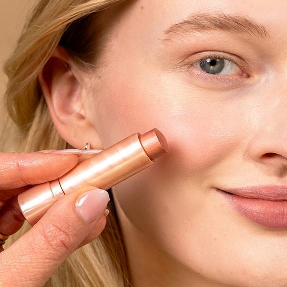 Nahaufnahme einer Frau beim Auftragen eines Rouge-Sticks auf die Wange