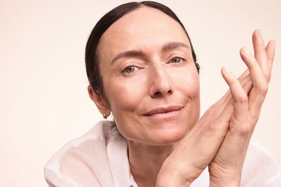 Reife Frau mit zurückgebundenem Haar vor warmem beigem Hintergrund